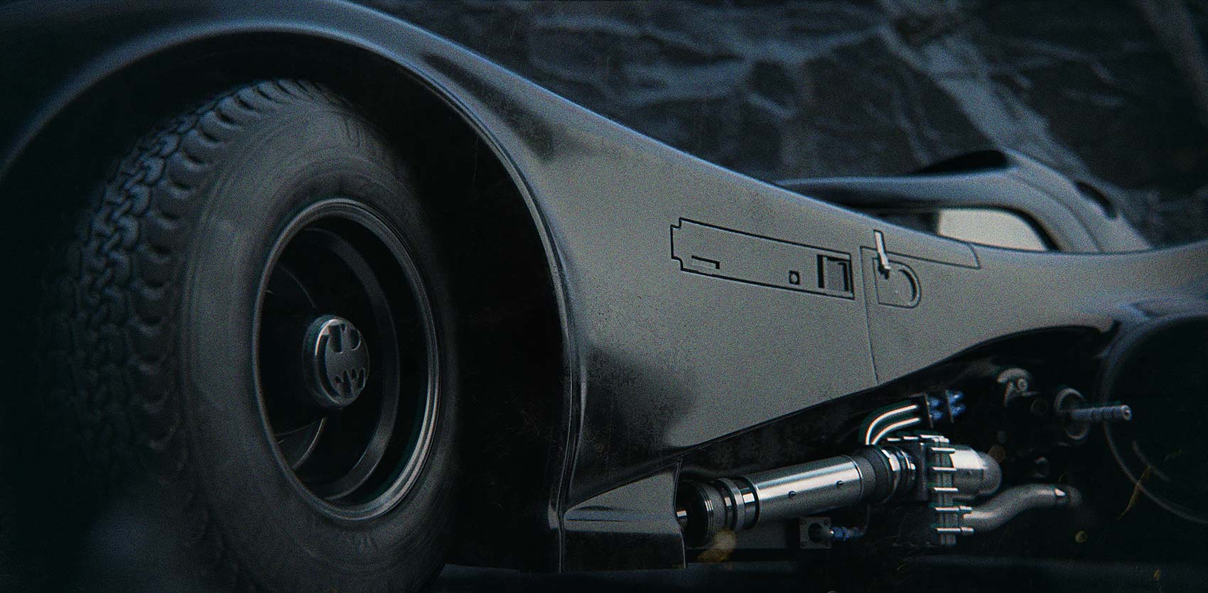 A macro close-up render of the Batmobile side panels, focusing on the textured rear tyre with the custom Bat-logo hubcap and the intricate, polished mechanical exhaust pipes and chassis detailing.