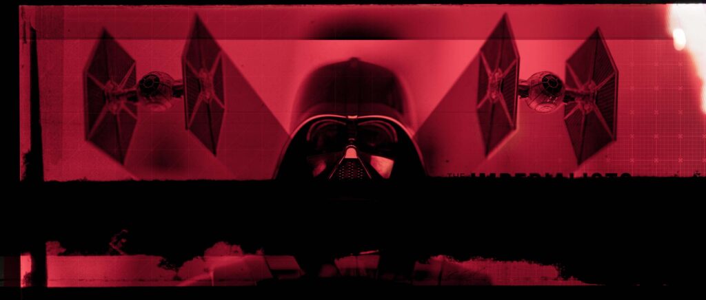 A striking symmetrical style frame featuring a central, front-facing 3D render of Darth Vader's helmet under crimson lighting, flanked on either side by a TIE Fighter asset, and divided horizontally by a thick, distressed black textured band across the lower half of the composition.