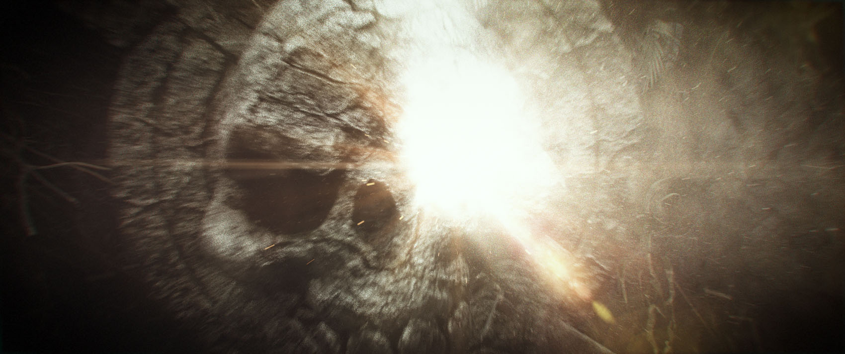 The final look-development frame in the sequence showing a powerful, hazy light burst illuminating the intricate cracks and degraded material details of the cavern's skull carving.
