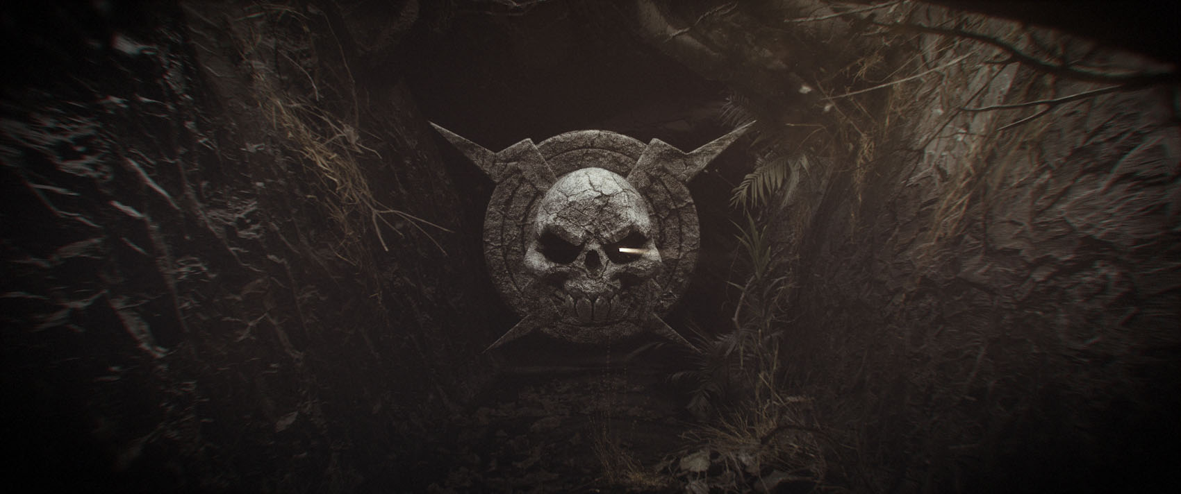 An atmospheric, wide film frame revealing a carved stone skull emblem inside a dark, rocky cavern hallway with sharp, textured stone walls.
